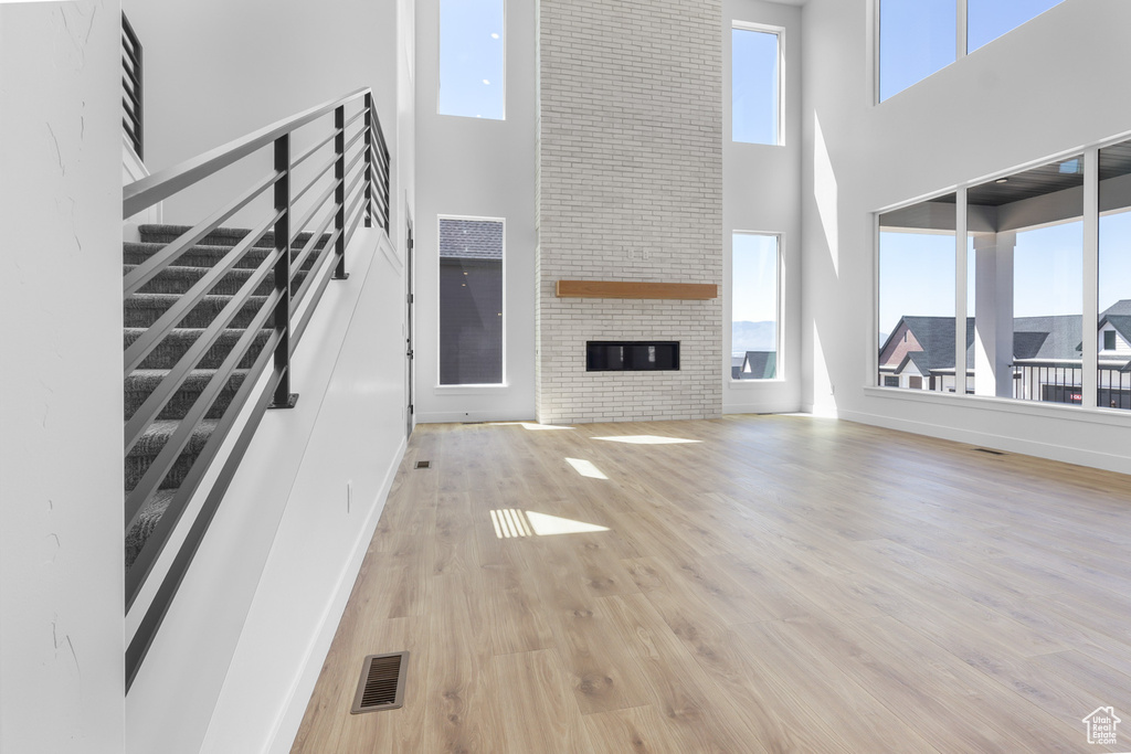 Unfurnished living room with a towering ceiling, light wood-style floors, stairs, and a large fireplace