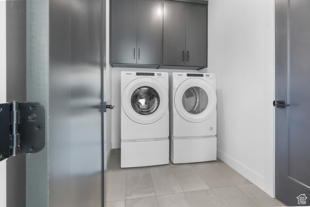 Laundry room with independent washer and dryer, cabinet space, light tile patterned floors, and baseboards