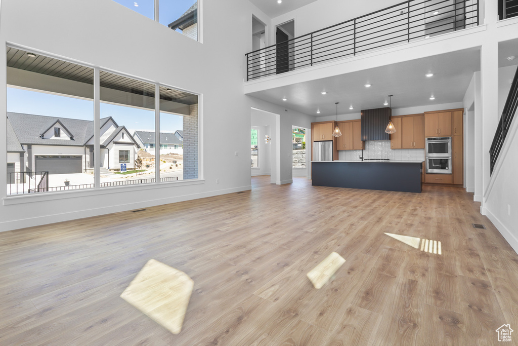 Unfurnished living room with light wood-style flooring, baseboards, and a towering ceiling