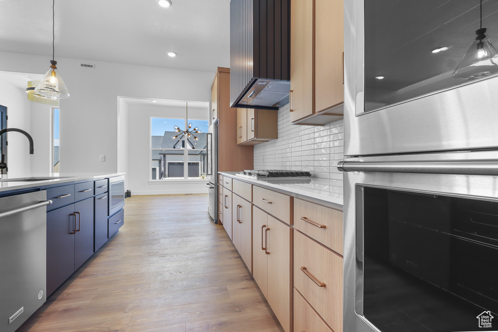 Kitchen featuring stainless steel appliances, a sink, wall chimney range hood, light wood-style flooring, and backsplash