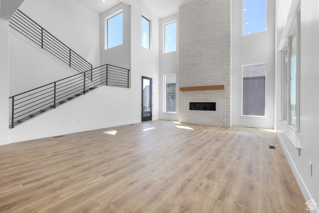 Unfurnished living room featuring a towering ceiling, stairs, baseboards, wood finished floors, and a fireplace