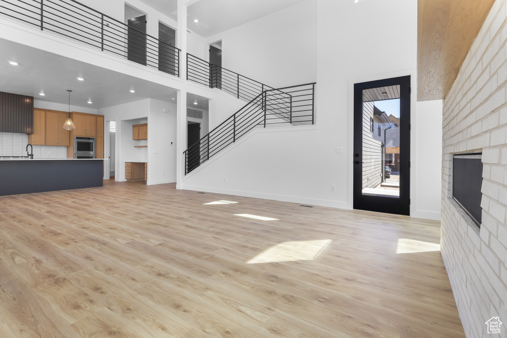 Unfurnished living room featuring a towering ceiling, a fireplace, light wood finished floors, baseboards, and stairway