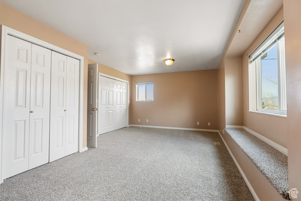 Unfurnished bedroom with baseboards, carpet floors, and two closets