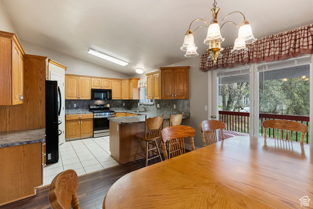 Kitchen featuring lofted ceiling, an inviting chandelier, light wood-type flooring, decorative backsplash, and black appliances