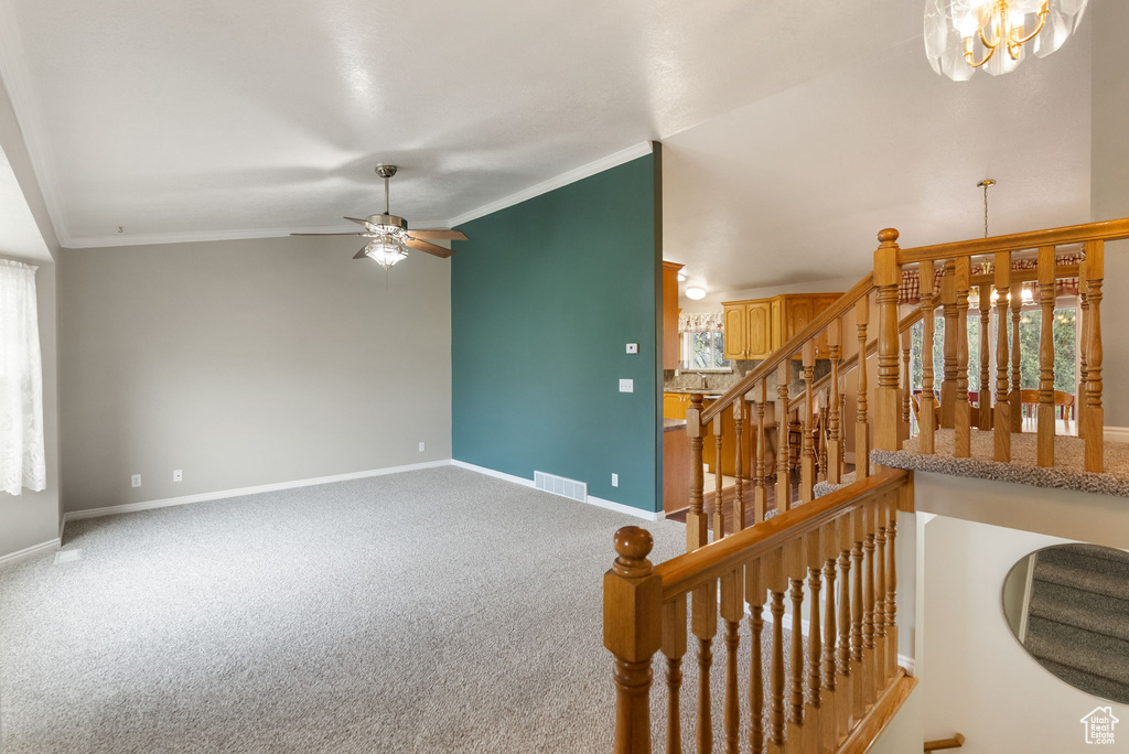 Interior space featuring visible vents, carpet floors, crown molding, baseboards, and ceiling fan with notable chandelier