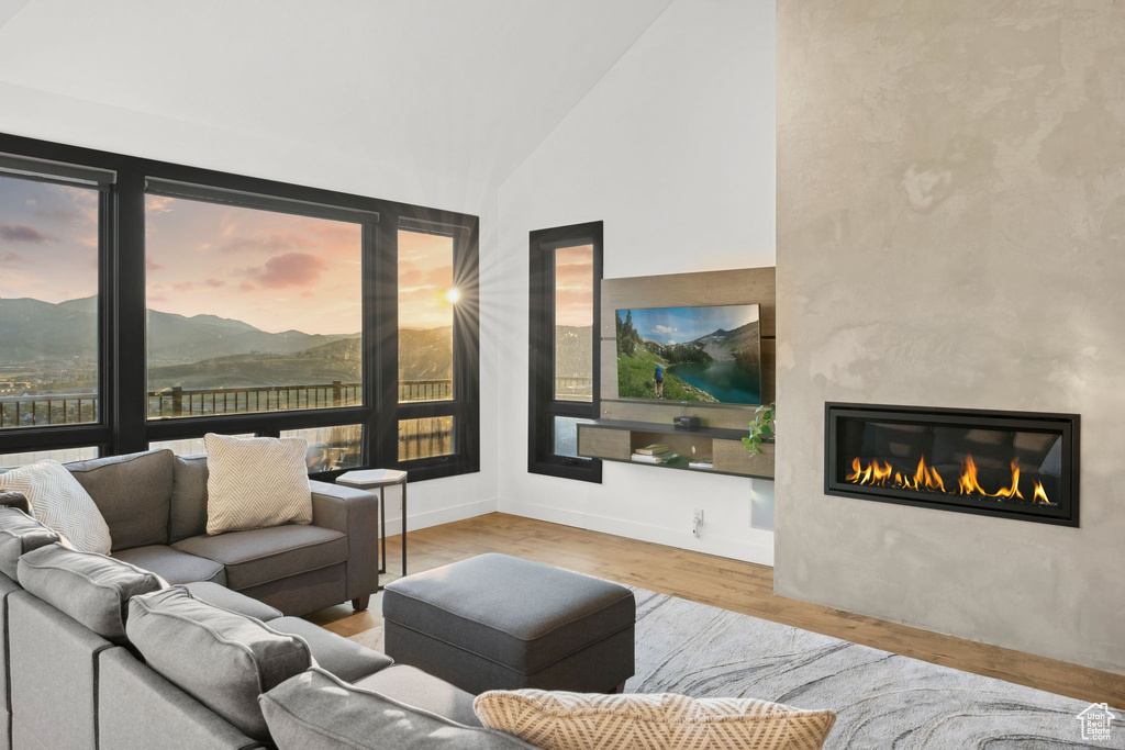Living area with baseboards, high vaulted ceiling, a glass covered fireplace, and wood finished floors