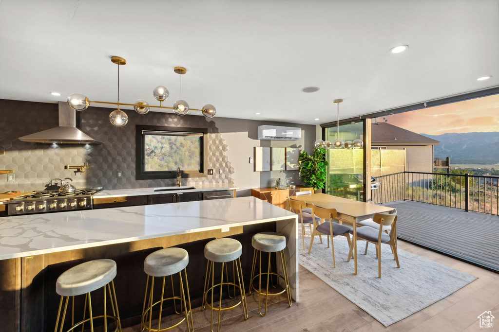 Kitchen with wall chimney exhaust hood, a sink, light stone countertops, decorative backsplash, and stainless steel gas cooktop