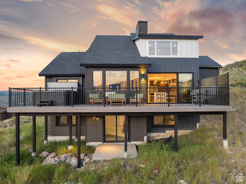 Back of property at dusk featuring a patio, a wooden deck, a chimney, and a shingled roof