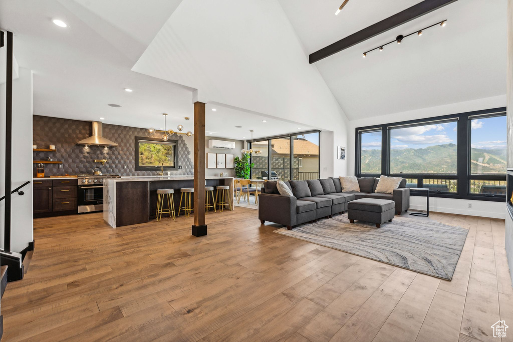 Living room featuring beamed ceiling, light wood-style flooring, high vaulted ceiling, and a wall mounted AC