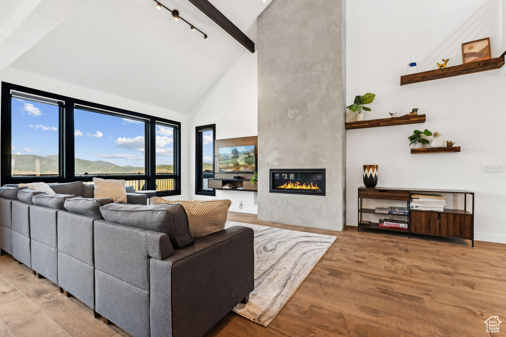 Living room featuring wood finished floors, high vaulted ceiling, a large fireplace, and beam ceiling