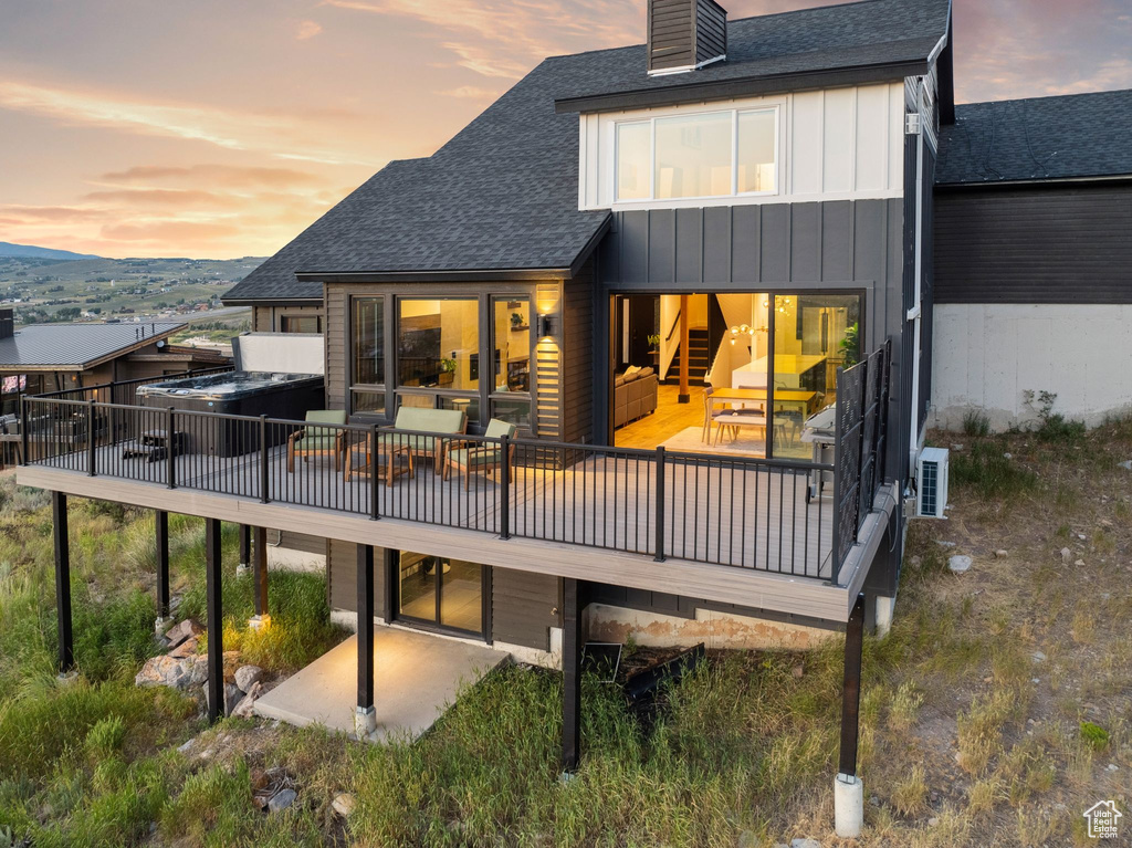 Back of property at dusk featuring a chimney, a wooden deck, a patio, and roof with shingles