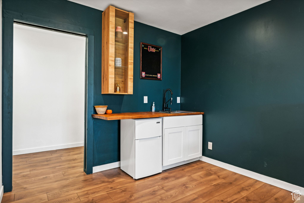 Bar with baseboards, a sink, light wood-type flooring, freestanding refrigerator, and wet bar