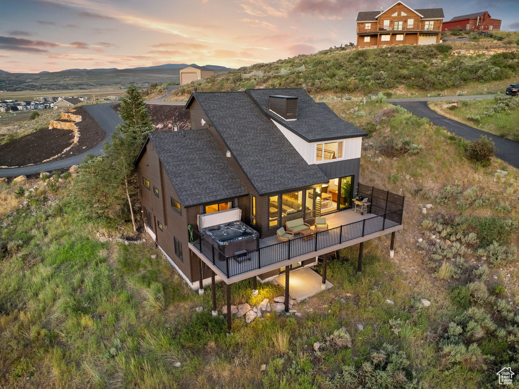 Back of property at dusk with a deck with mountain view and a shingled roof