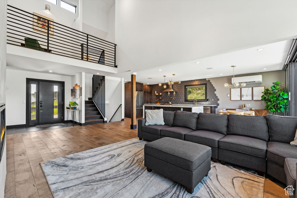 Living area featuring a towering ceiling, stairway, a wall mounted AC, wood finished floors, and plenty of natural light