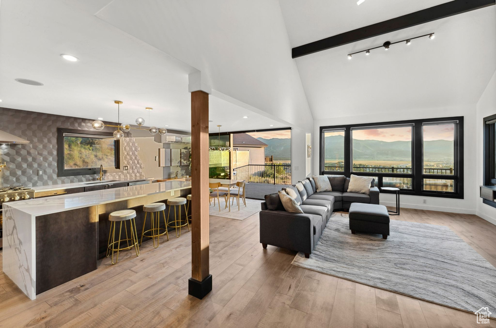 Living area with high vaulted ceiling, light wood-type flooring, wallpapered walls, baseboards, and beam ceiling