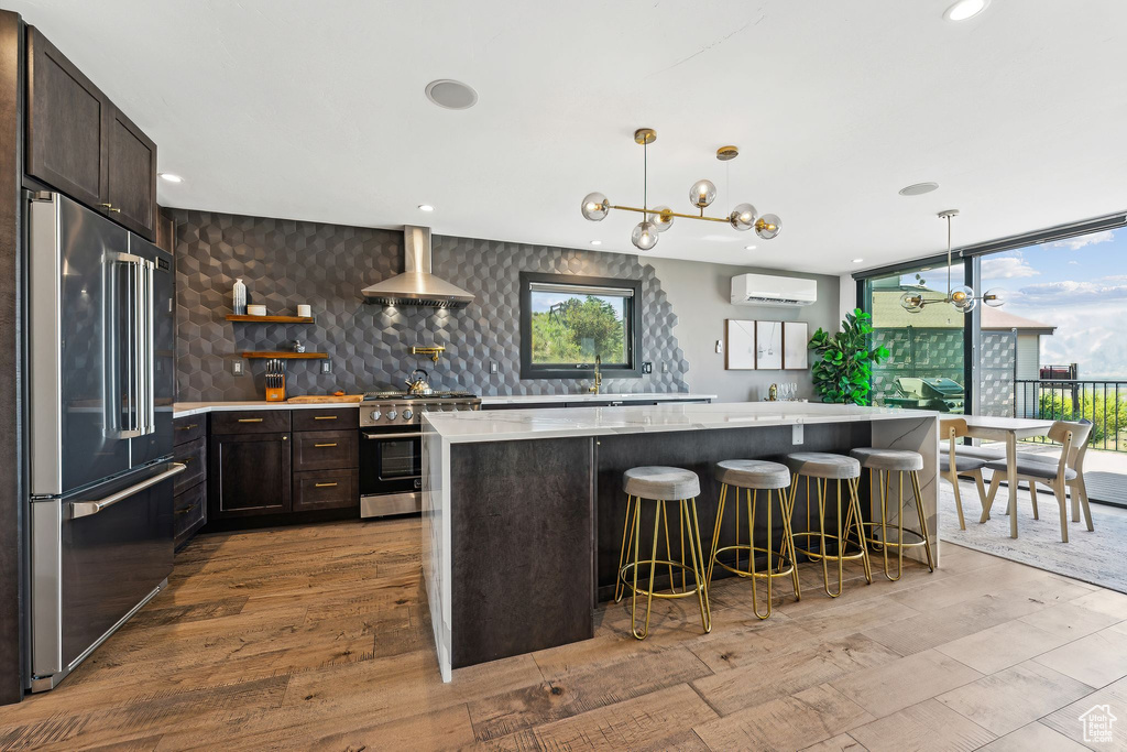 Kitchen featuring wall chimney range hood, light countertops, an AC wall unit, dark brown cabinets, and high end appliances
