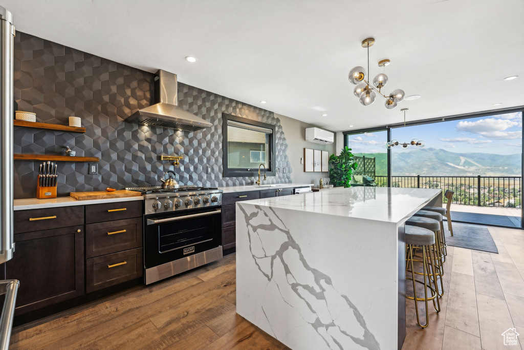 Kitchen with wall chimney exhaust hood, floor to ceiling windows, a wall mounted AC, stainless steel stove, and light stone counters
