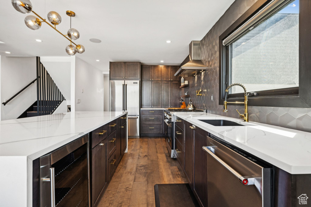 Kitchen with high quality appliances, dark wood-type flooring, wall chimney exhaust hood, beverage cooler, and a sink
