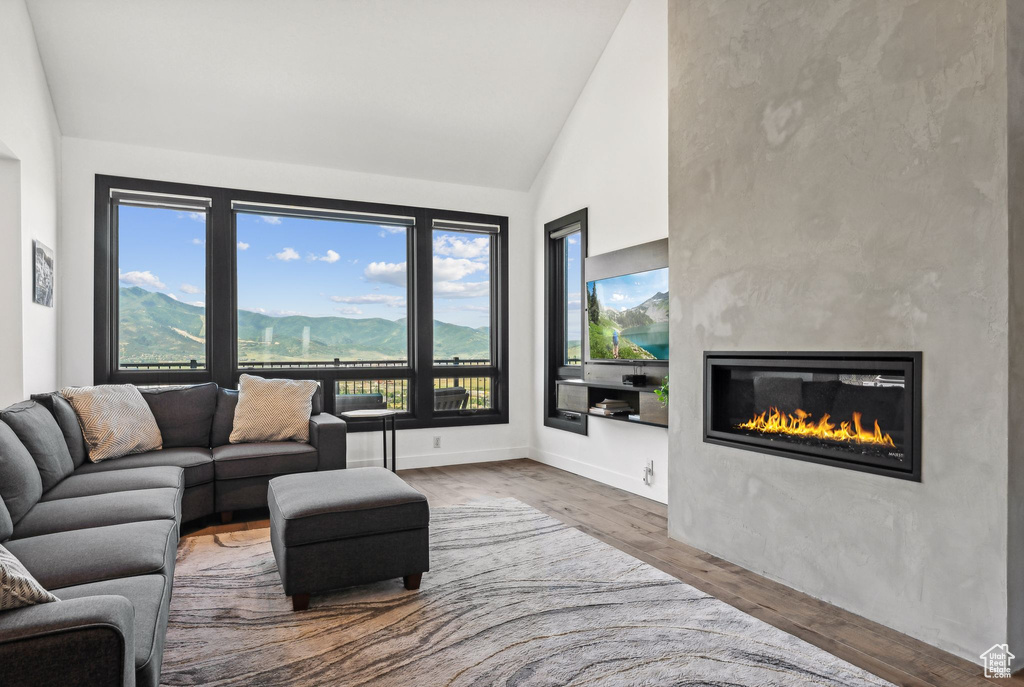 Living room with a glass covered fireplace, high vaulted ceiling, baseboards, and wood finished floors