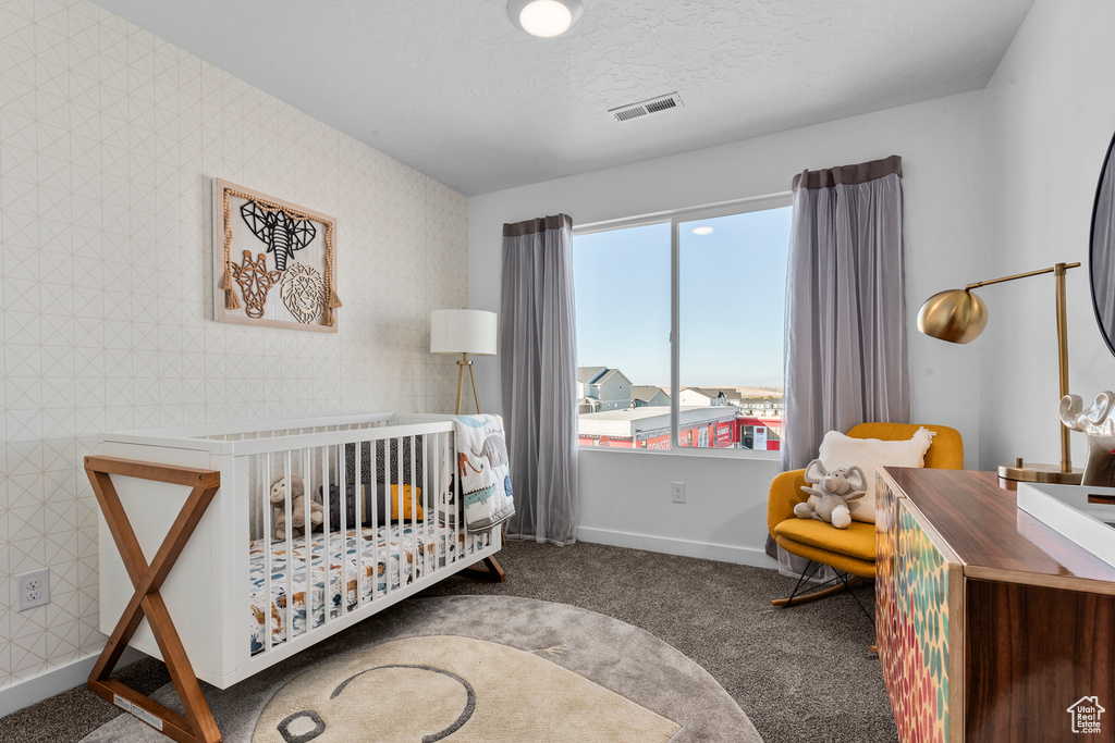 Bedroom with visible vents, baseboards, a crib, carpet floors, and wallpapered walls