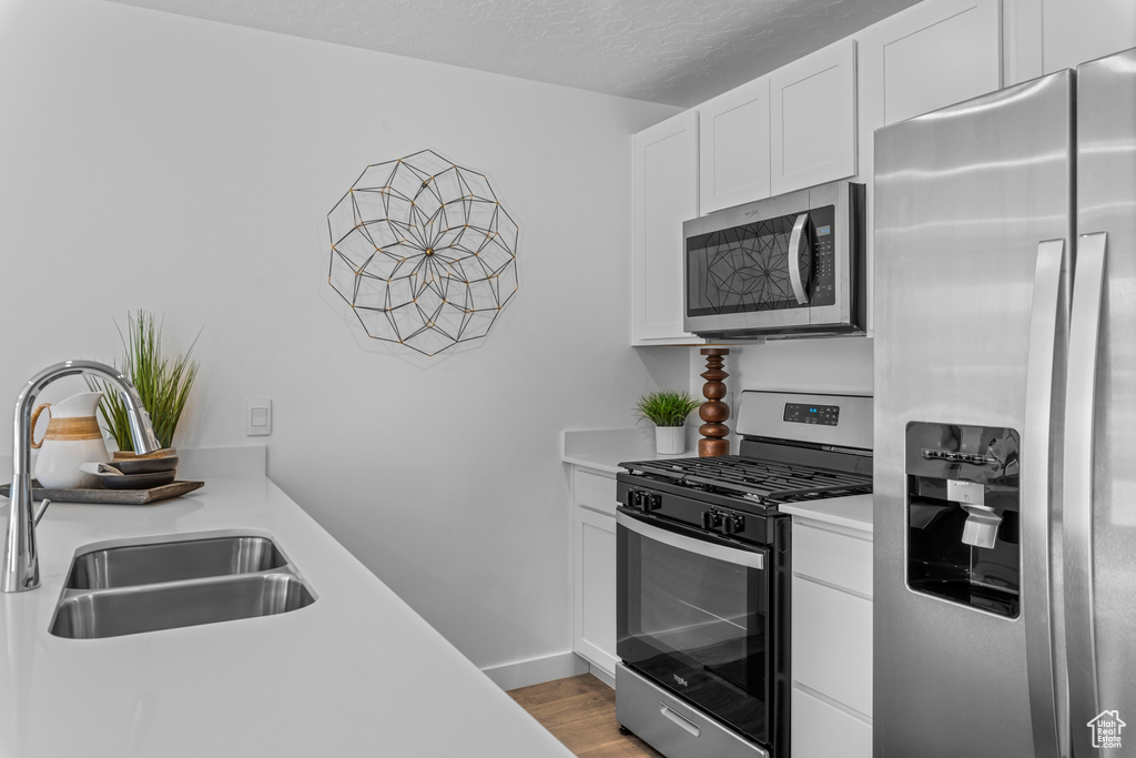 Kitchen featuring light wood-type flooring, light countertops, white cabinets, appliances with stainless steel finishes, and a sink