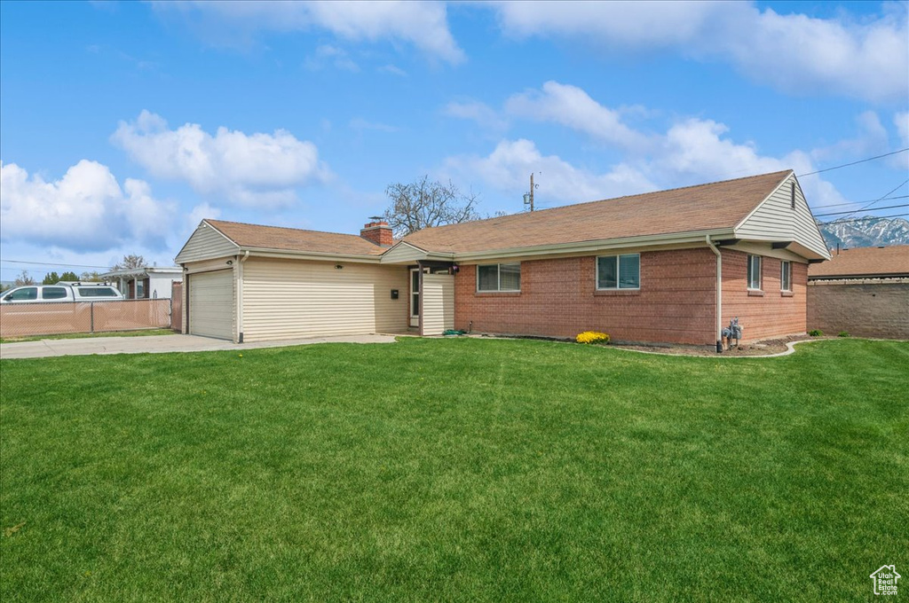 Ranch-style home featuring an attached garage, a chimney, concrete driveway, and a front lawn
