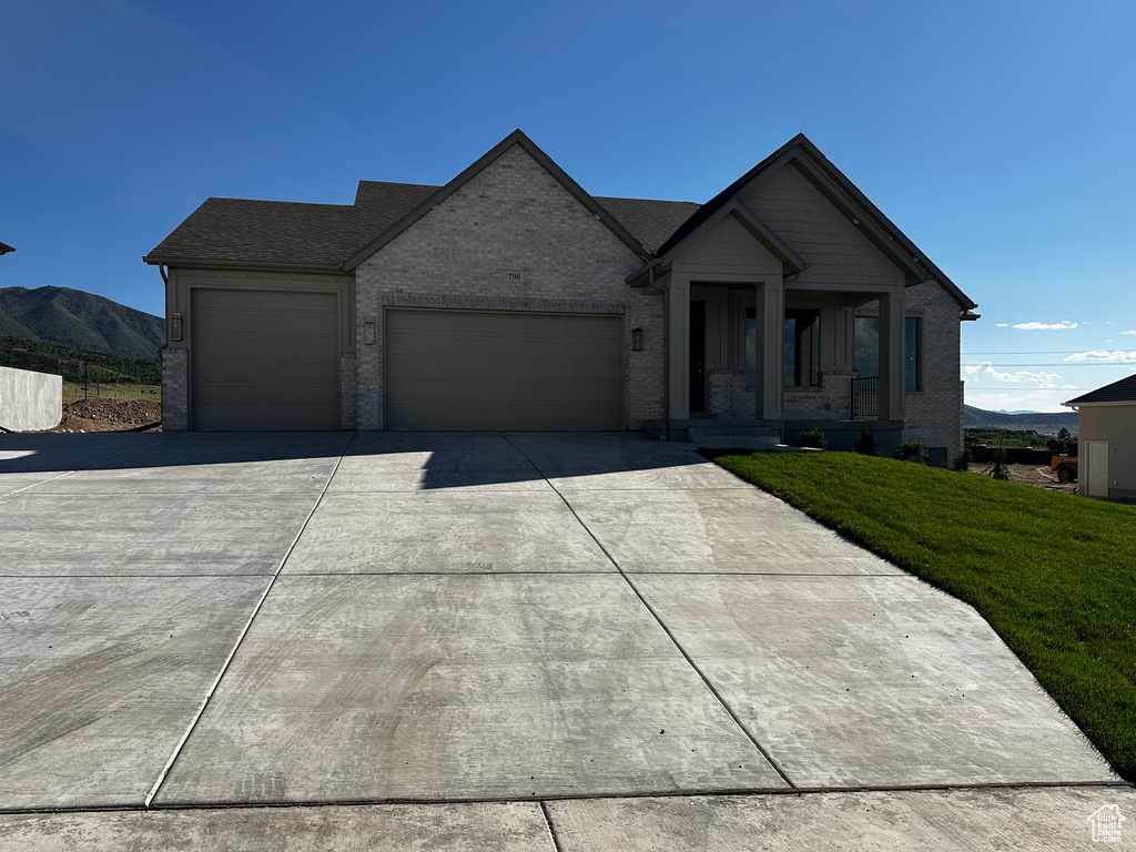 View of front of property with a garage, concrete driveway, brick siding, a front lawn, and a mountain view