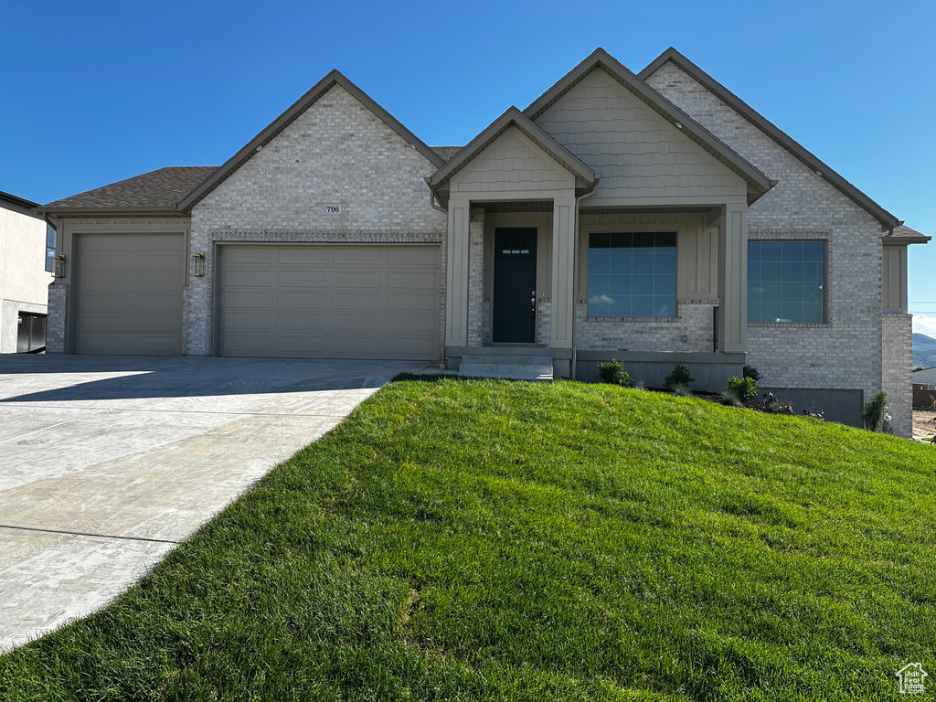 View of front of home with an attached garage, brick siding, a front yard, driveway, and board and batten siding