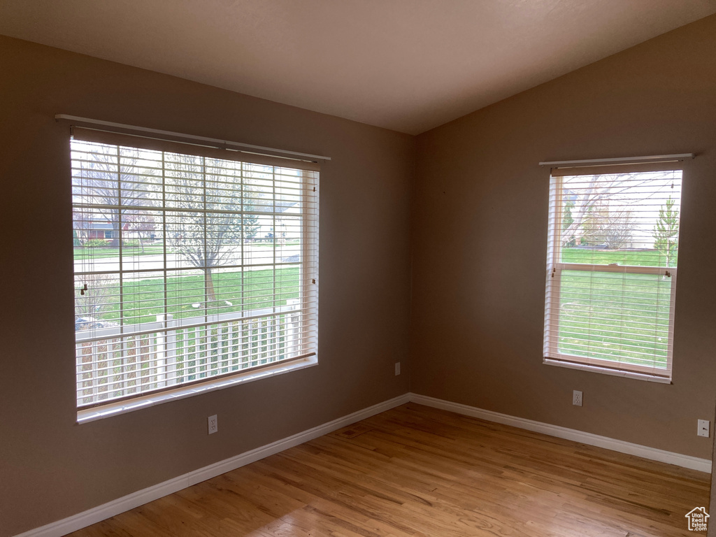 Spare room featuring wood finished floors, baseboards, vaulted ceiling, and a healthy amount of sunlight