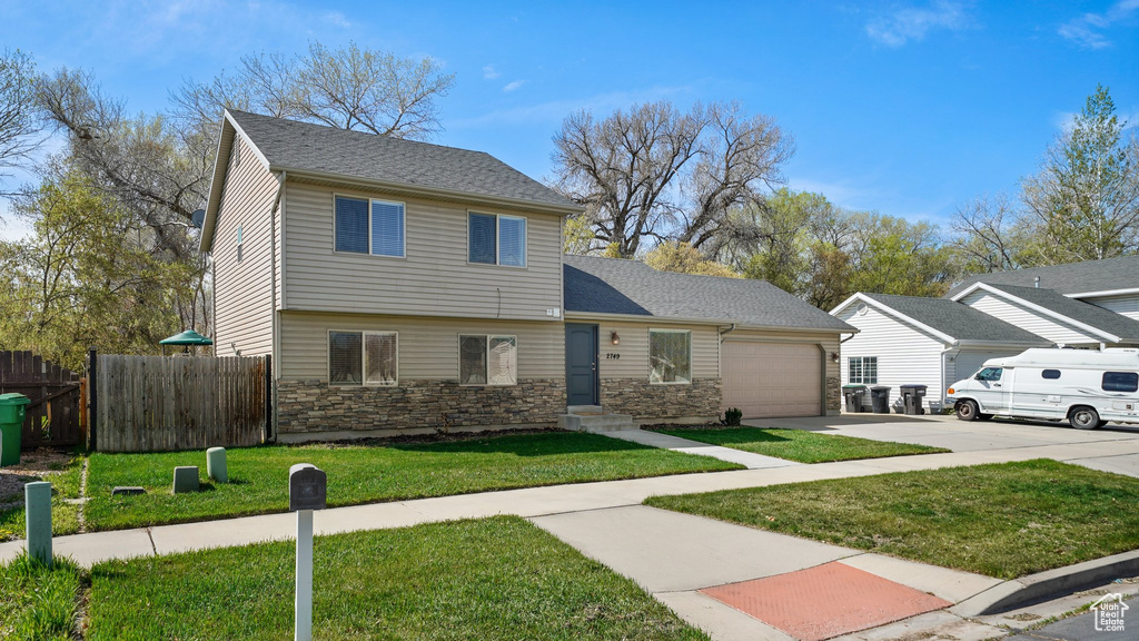 View of front of property featuring an attached garage, stone siding, fence, concrete driveway, and a front lawn