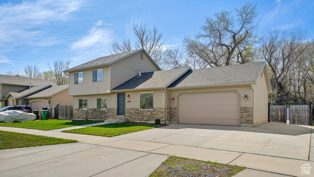 View of front of property with an attached garage, stone siding, fence, a gate, and driveway