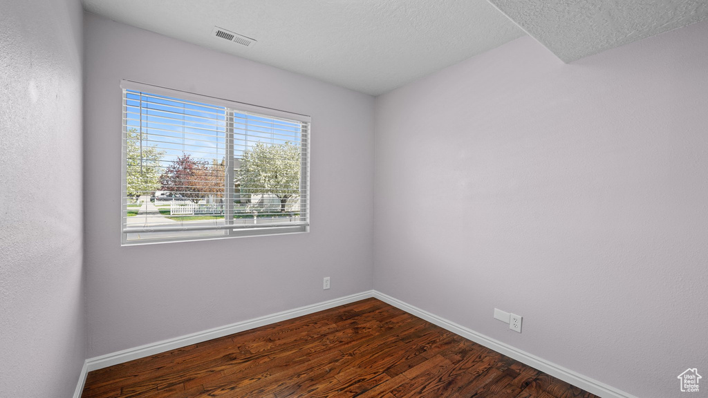 Unfurnished room featuring dark wood-style flooring, baseboards, and visible vents
