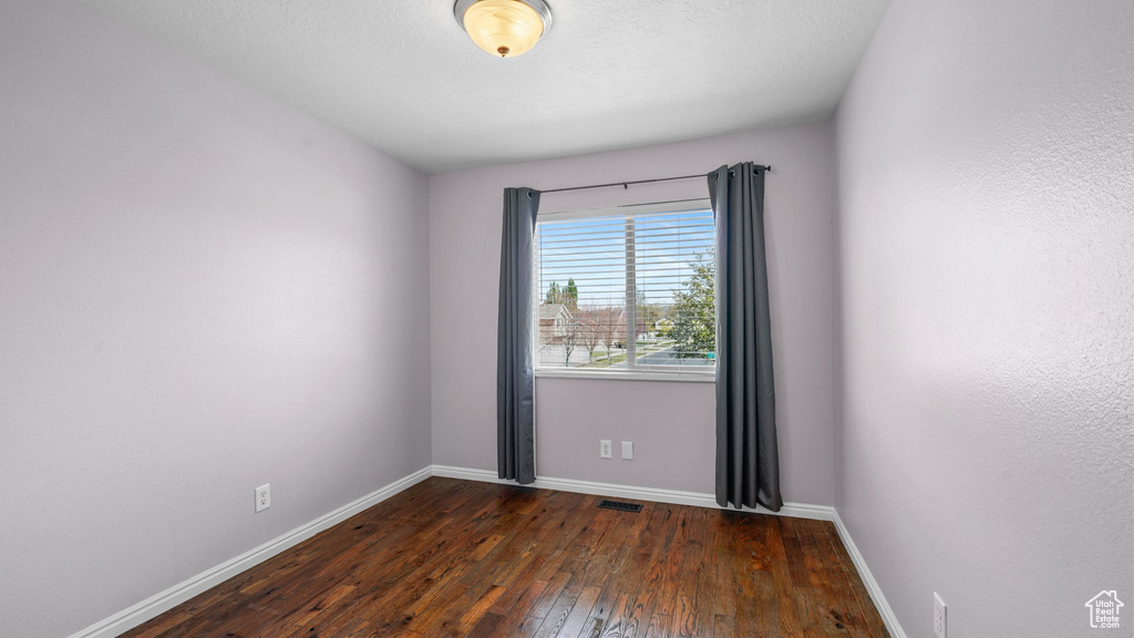 Empty room featuring dark wood-type flooring, visible vents, and baseboards