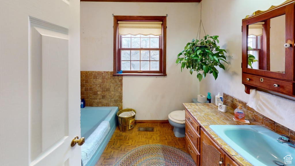 Full bathroom with visible vents, baseboards, toilet, a tub, and vanity