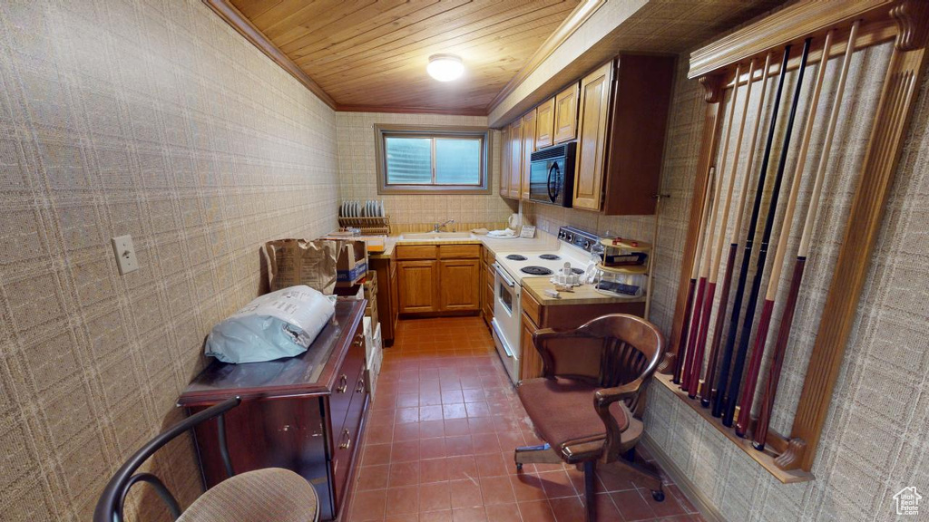 Kitchen featuring crown molding, black microwave, electric range, dark tile patterned flooring, and light countertops