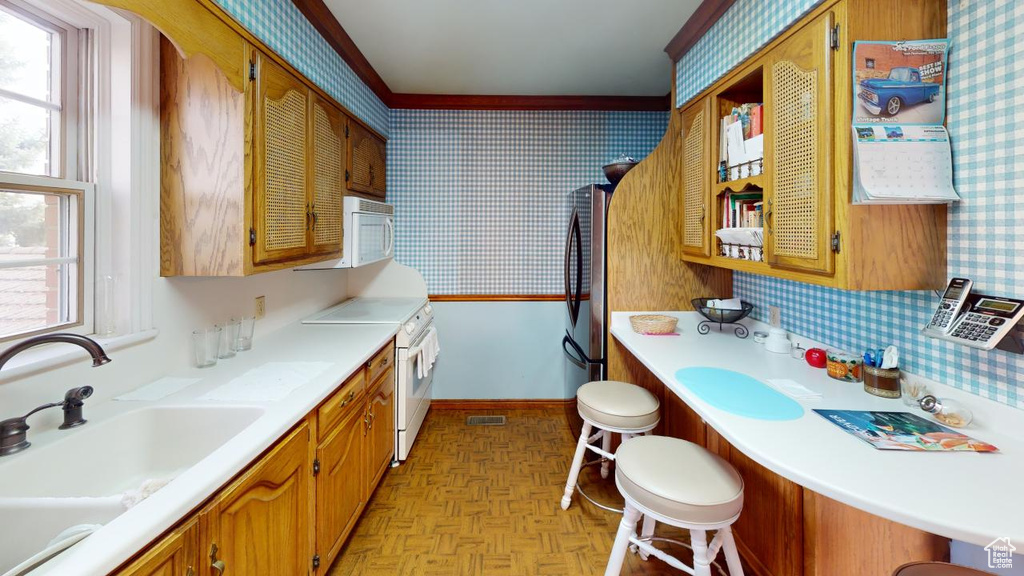Kitchen featuring baseboards, wallpapered walls, white appliances, light countertops, and a sink