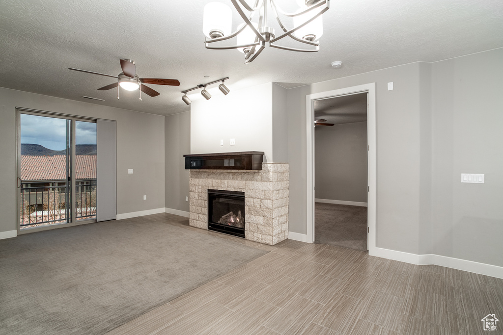 Unfurnished living room featuring baseboards, a textured ceiling, a fireplace, and ceiling fan with notable chandelier