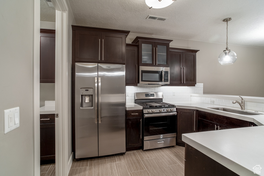 Kitchen with light countertops, stainless steel appliances, a sink, visible vents, and dark brown cabinetry