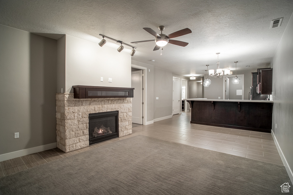 Unfurnished living room featuring a textured ceiling, a stone fireplace, baseboards, ceiling fan with notable chandelier, and visible vents