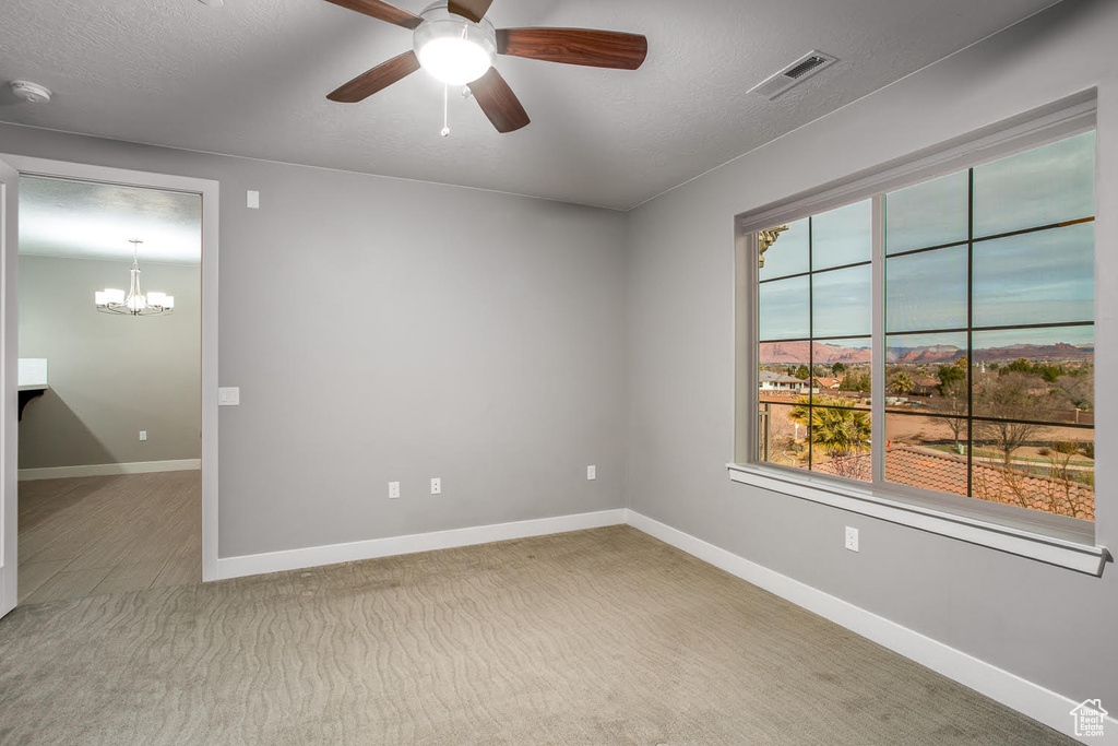 Empty room featuring baseboards, a textured ceiling, visible vents, and ceiling fan with notable chandelier