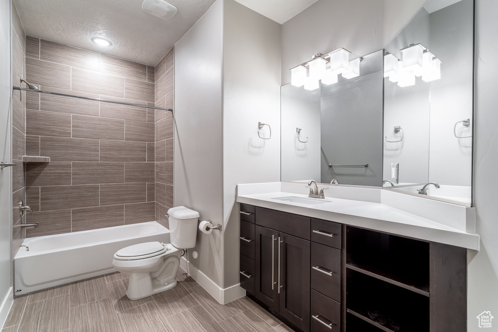 Full bath with vanity, toilet, baseboards, a textured ceiling, and shower / bathtub combination
