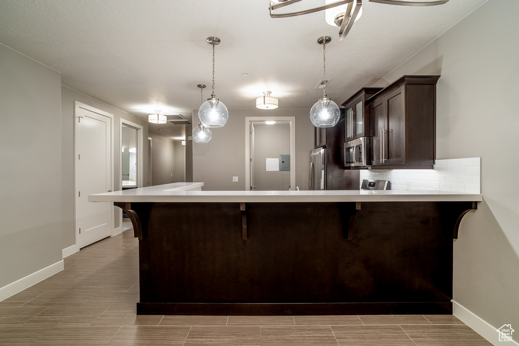 Kitchen with dark brown cabinetry, light countertops, a breakfast bar area, and appliances with stainless steel finishes