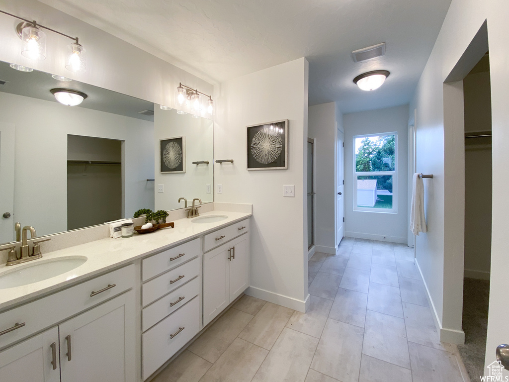Full bath featuring a sink, a spacious closet, double vanity, and baseboards