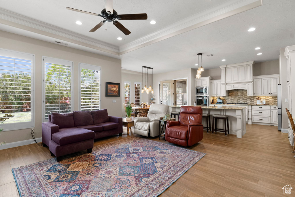 Living area with a tray ceiling, crown molding, ceiling fan, and a wealth of natural light