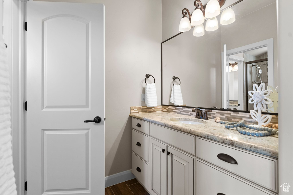 Bathroom featuring vanity, a shower with door, a chandelier, decorative backsplash, and baseboards