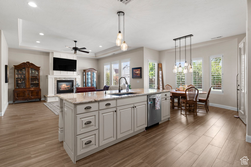 Kitchen featuring dishwasher, a sink, a stone fireplace, a tray ceiling, and ceiling fan with notable chandelier
