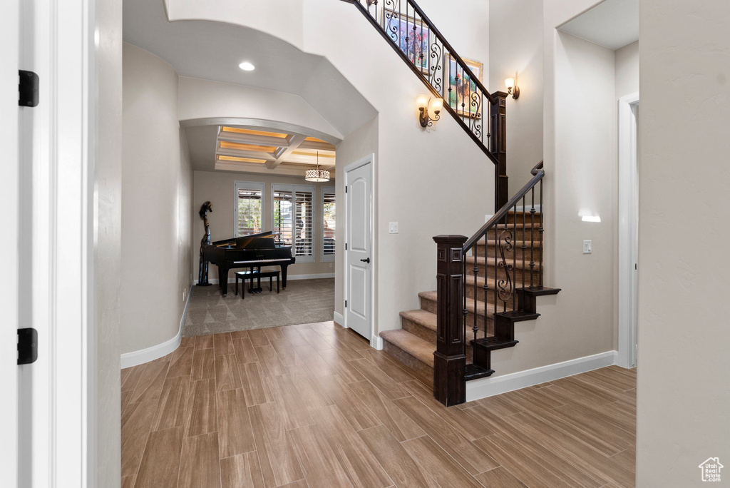 Foyer entrance featuring baseboards, arched walkways, light wood finished floors, stairway, and coffered ceiling