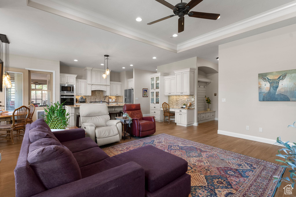 Living area featuring crown molding, ceiling fan, wood finished floors, a raised ceiling, and baseboards