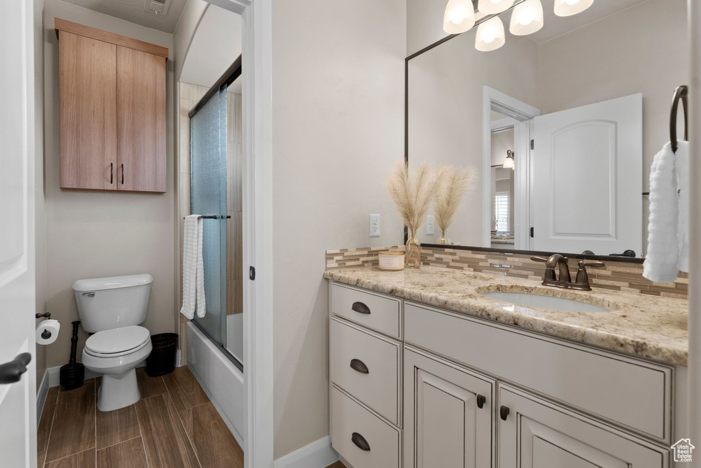 Bathroom featuring vanity, toilet, enclosed tub / shower combo, wood tiled floor, and baseboards
