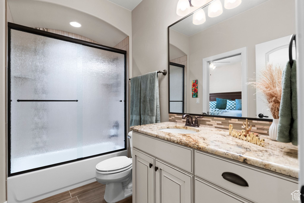 Ensuite bathroom featuring tasteful backsplash, vanity, enclosed tub / shower combo, toilet, and connected bathroom